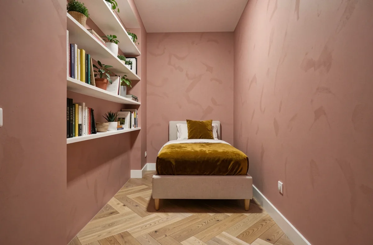 Chambre étroite aux murs rose poudré avec étagères blanches encastrées et parquet chêne en chevrons, montrant comment une couleur enveloppante évite l'effet boîte dans un petit espace
