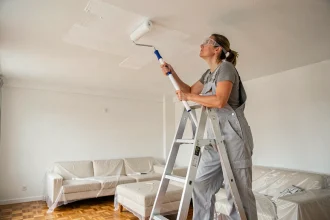 Femme appliquant de la peinture action blanche sur un plafond avec un rouleau à manche télescopique dans un salon moderne