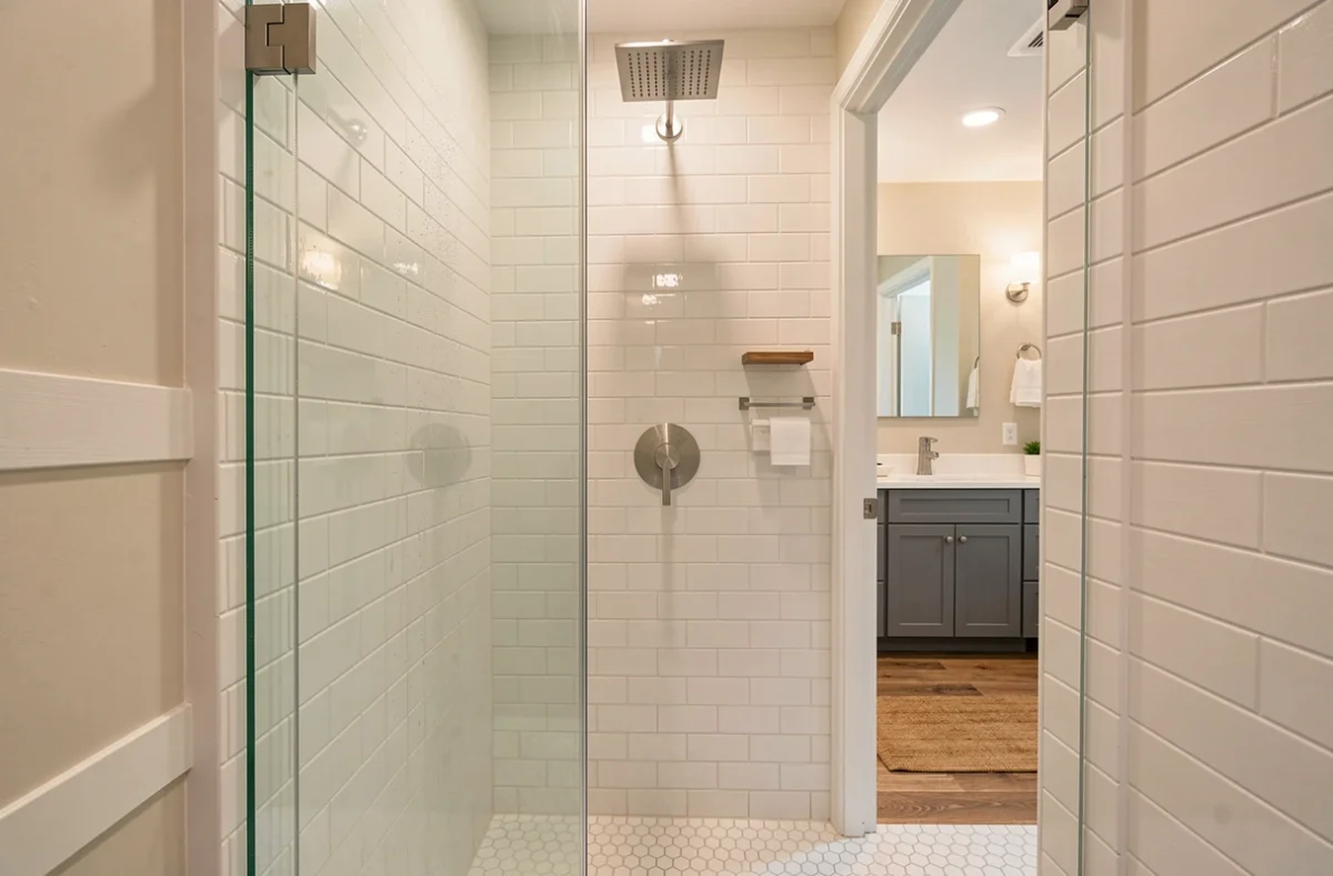 Cabine de douche fermée avec mitigeur en nickel brossé monté à hauteur adulte sur carrelage métro blanc et pommeau encastré au plafond