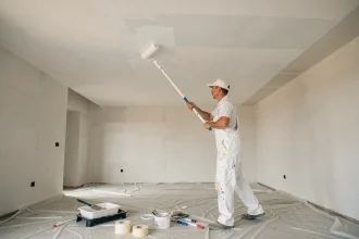 Peintre professionnel appliquant de la peinture blanche au rouleau sur un plafond de maison neuve de 50m2